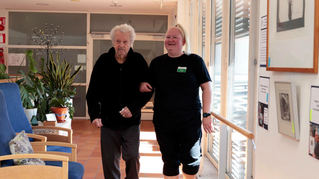 Kuvassa Wilhelmiinan asukas ja työntekijä kävelevät hoivakodin käytävällä.